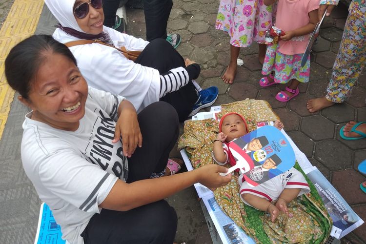 Verawati (35) sedang mengipasi anaknya yang sesang kepanasan dilokasi kampanye Prabowo di pelataran Benteng Kuto Besak Palembang, Sumatera Selatan, Selasa (9/4/2019).