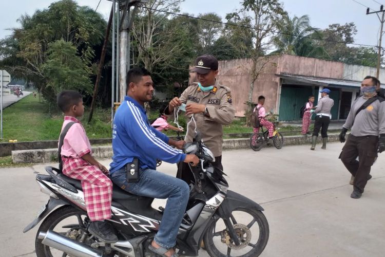 Kapolsek Rupat AKP Masrial membagikan masker kepada salah seorang pengendara sepeda motor di Jalan Pelajar, Kelurahan Batu Panjang, Kecamatan Rupat, Kabupaten Bengkalis, Riau, Kamis (21/2/2019). Pembagian masker ke masyarakat untuk mengantisipasi dampak dari kabut asap karhutla yang terjadi di wilayah Kecamatan Rupat tersebut. 