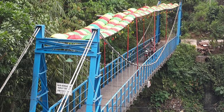 Seorang pengendara saat melintas di atas jembatan gantung di RT 6 RW 5 Kelurahan Penanggungan, Kecamatan Klojen, Kota Malang, Jawa Timur, Selasa (14/11/2017). Jembatan itu dihias dengan payung supaya kelihatan lebih indah.