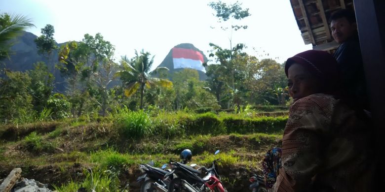 Seorang warga menyaksikan bendera raksasa di Puncak Gunung Buchu, Sekitar Gunung Api Purba Nglanggeran, Patuk, Gunungkidul, DI Yogyakarta, Senin (13/8/2018). 