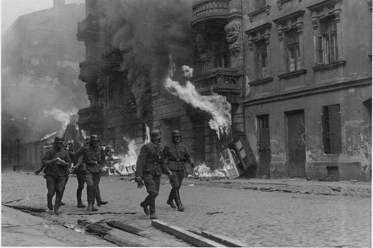 Sekelompok prajurit Jerman berjalan melintasi sebuah bangunan yang terbakar di ghetto Warsawa, Polandia.