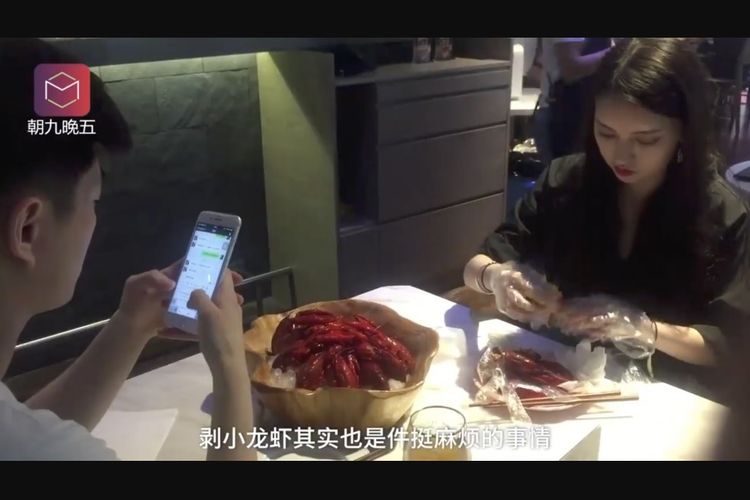 He Nanxin (kanan) mengupas udang karang, sementara seorang pelanggan restoran tetap bermain ponsel.
