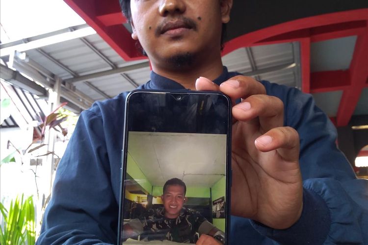 Dita Ibnu Ariandana menunjukkan foto adiknya, Serda Dita Ilham Primojati (24), salah satu kru helikopter TNI AD yang hilang di Papua, Sabtu (29/6/2019).