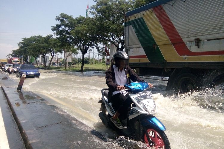 Seorang pengendara motor melintasi genangan air di Jalur Pantura Kilometer 14,  Onggorawe, Sayung, Selasa (9/4/2019)