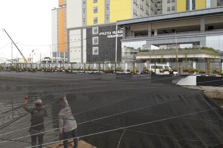 Aliran Limbah Dua orang pekerja melintas di bawah jaring berwarna hitam yang menutupi Kali Item dekat Wisma Atlet Kemayoran, Kamis (19/7/2018).