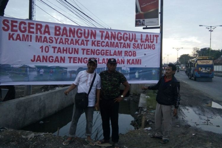 Spanduk bernada protes terpasang  di jalur Pantura Sayung,  Demak,  agar segera dibangun tanggul laut untuk antisipasi banjir rob,  Minggu (5/12/2017)