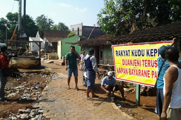 Warga yang rumah dan tanaknya terkena proyek tol memasang spanduk di Protomulyo kendal, sebagai bentuk protes keterlambatan pembayaran ganti rugi.