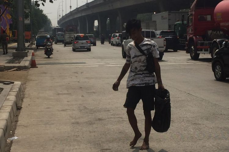 Manto menenteng kantong plastik berisi oli yang ia ambil dari truk tangki yang tengah melintas di Jalan Yos Sudarso, Jakarta Utara, Selasa (2/7/2018).
