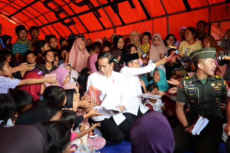 Presiden Joko Widodo (Jokowi) dan Gubernur NTB Tuan Guru Bajang Zainul Majdi (TGB) membagikan buku untuk para pengungsi di Lombok, NTB, Minggu (2/9/2018)
