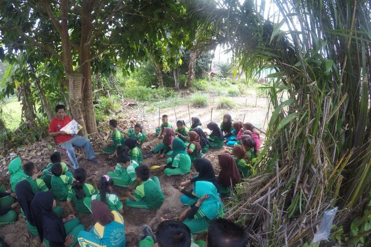 Yosep membacakan cerita kepada anak-anak di ladang sekolah, disela-sela waktu istirahat. Yosep merawat nasionalisme di pedalaman Kaltara dengan mendekatkan buku kepada anak.