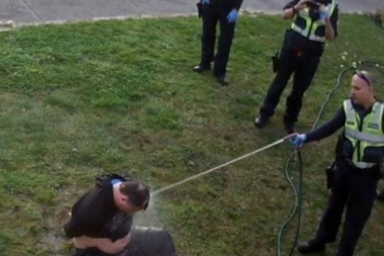 Seorang polisi menyemprotkan air ke wajah John yang merupakan penyandang disabilitas.