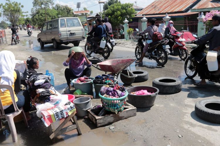 Nurhayati dan beberapa wanita Baliase, Kabupaten Sigi, memanfaatkan air dari pipa PDAM yang pecah di pinggir jalan untuk mencuci.