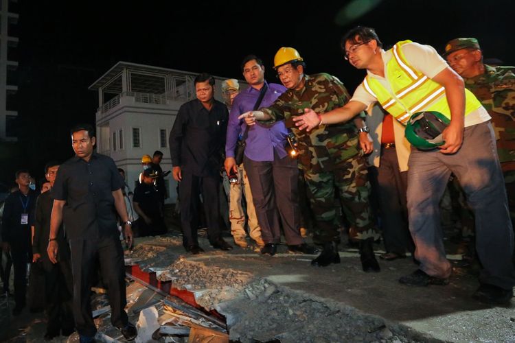 Perdana Menteri Kamboja Hun Sen (tengah, berseragam militer) meninjau lokasi bangunan ambruk di Sihanoukville Minggu (23/6/2019). Sekitar 24 orang dilaporkan tewas setelah bangunan tujuh lantai itu runtuh Sabtu (22/6/2019).