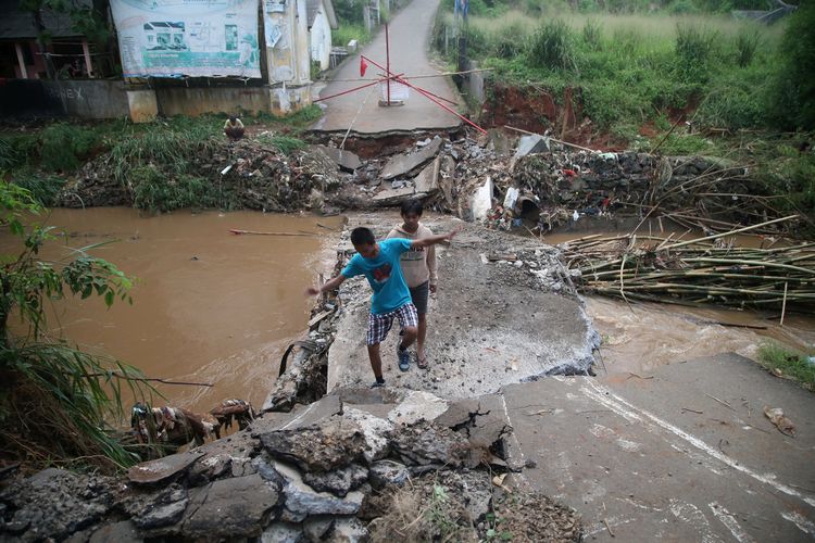 Warga melintasi jembatan yang putus akibat diterjang banjir Kali Angke, di dekat Villa Pamulang, Tangerang Selatan, Banten, Minggu (19/4/2020). Banjir yang terjadi pada Sabtu (18/4/2020) itu berasal dari kawasan hulu.