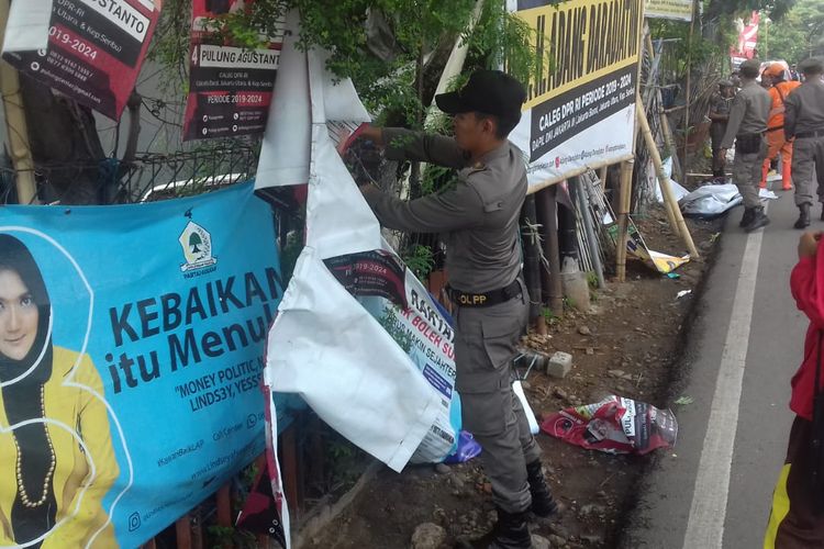 Petugas Satpol PP menurunkan sejumlah alat peraga kampanye yang melanggar aturan di Kecamatan Koja, Kamis (14/3/2019).