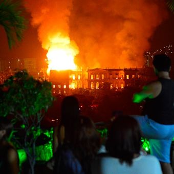 Warga menyaksikan api yang melalap gedung museum nasional Brasil di Rio de Janeiro, Minggu (2/9/2018). Bangunan ini merupakan institusi sains tertua di negeri itu.