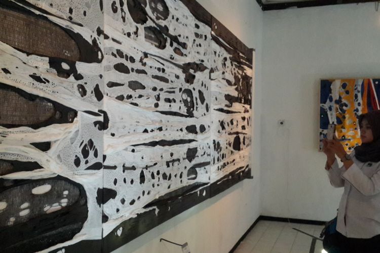 Seorang pengunjung sedang melihat salah satu karya lukisan dengan medium plastik kresek hasil kreasi Masari Arifin yang dipamerkan di Gedung Dewan Kesenian Malang (DKM), Selasa (5/12/2017).