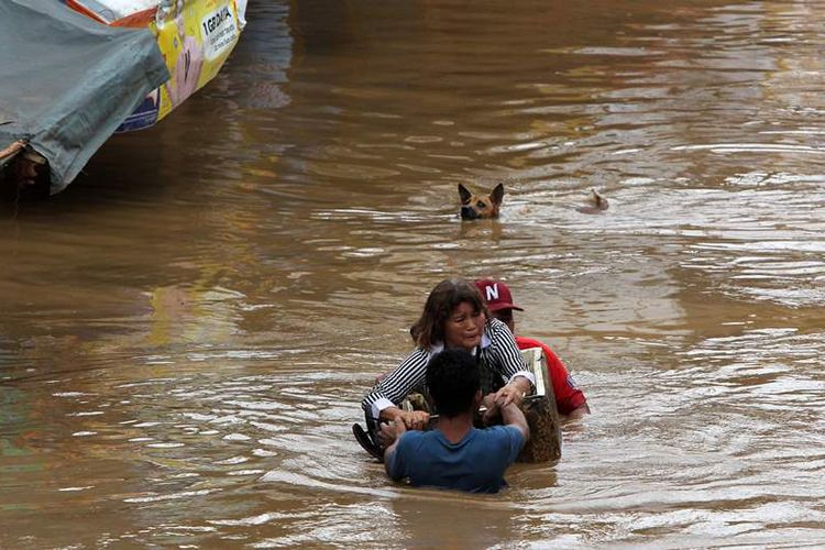 Seorang penduduk dibantu dua pria berusaha mengarungi jalan yang banjir di Cagayan City pada 22 Desember 2017, setelah Sungai Cagayan meluap akibat hujan lebat yang ditimbulkan oleh Badai Tropis Tembin. (AFP via Strait Times)