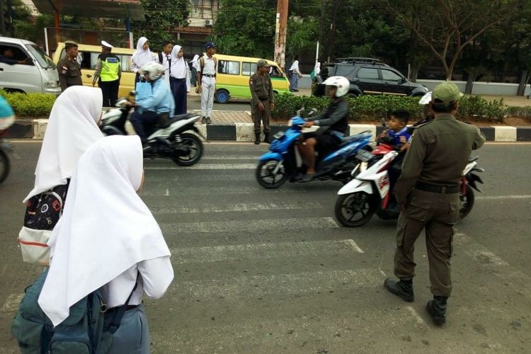 Personel Satpol PP sedang membantu siswa-siswi menyeberang di Jalan Ahmad Yani Karawang.