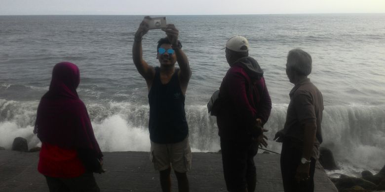 Mengabadikan foto di tepi jurang di ujung jalan beton pemecah ombak di Pantai Glagah, Kulon Progo, demi memperoleh latar ombak besar, memang menantang. Tapi pengunjung mesti hati-hati karena di situ area berbahaya. Tepian ujung jalan itu tanpa pengaman. 