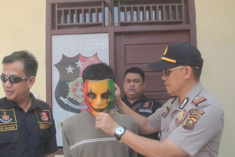 Kapolsek Indralaya AKP Bambang Julianto mengenakan topeng ke tersangka RK. Topeng tersebut digunakan RK saat beraksi menjambret telepon genggam seorang mahasiswa Unsri Indralaya di Simpang Timbangan Indralaya, Ogan Ilir, Sumsel, Kamis (7/6/2018). 