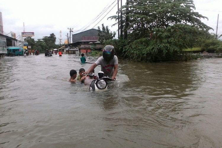 Warga terpaksa mendorong motornya dengan menembus banjir di Kelurahan Katimbang, Kecamatan Biringkanaya, Makassar, Kamis (21/12/2017).