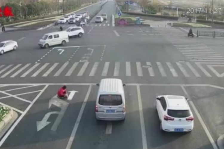 Pria di China berbaju merah tampak sedang membuat garis marka di persimpangan jalan yang ramai.