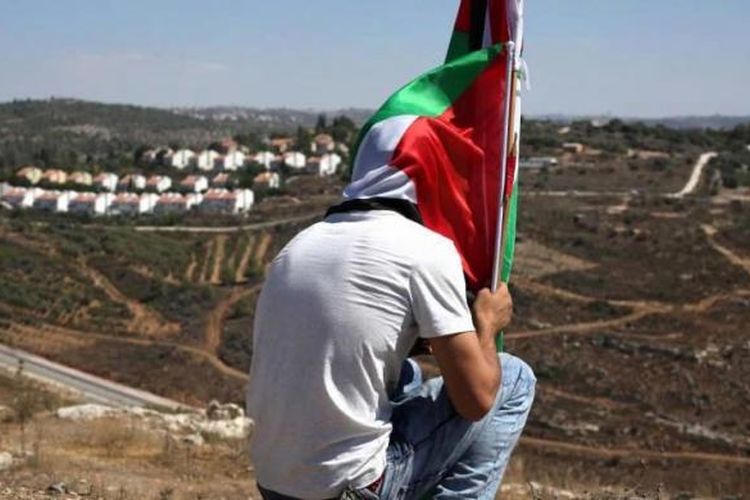Seorang demonstranduduk sambil memegang bendera Palestina setelah aksi melawan perampasan tanah Palestina untuk memperluas pemukiman Yahudi Hallamish (latar belakang), Jumat (28/8/2015), di Desa Nabi Saleh, Tepi Barat, dekat Ramallah.