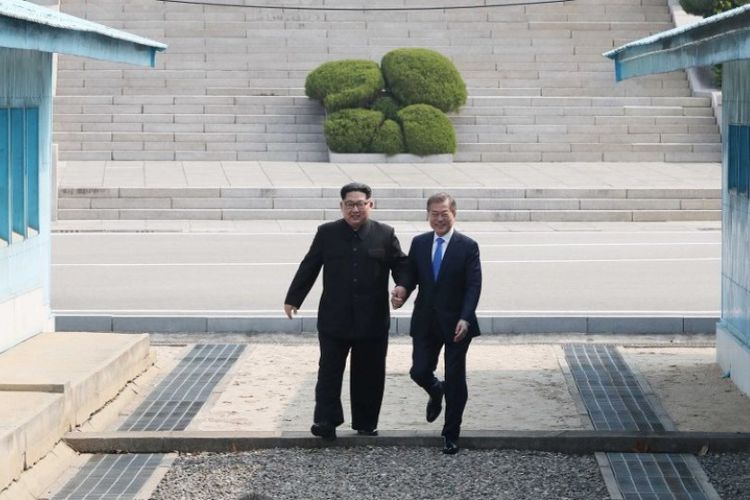 Pemimpin Korea Utara Kim Jong Un (kiri) melangkah bersama Presiden Korea Selatan Moon Jae-in (kanan) melintasi Garis Demarkasi Militer yang membagi negara mereka, menjelang pertemuan di Gedung Perdamaian resmi di Panmunjom, Jumat (27/4/2018).