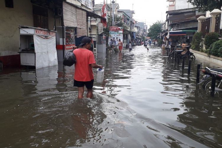 Seorang warga melintas di Jalan Kerapu 3 Muara Angke yang terendam banjir, Jumat (25/1/2019).