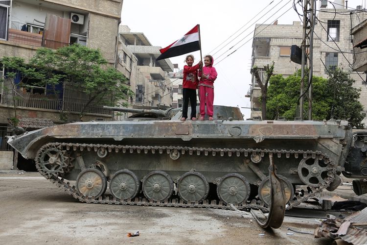 Anak-anak Suriah membawa bendera sambil berdiri di atas kendaraan tempur di wilayah Ghouta Timur, di Hazzeh, pinggiran Damaskus.