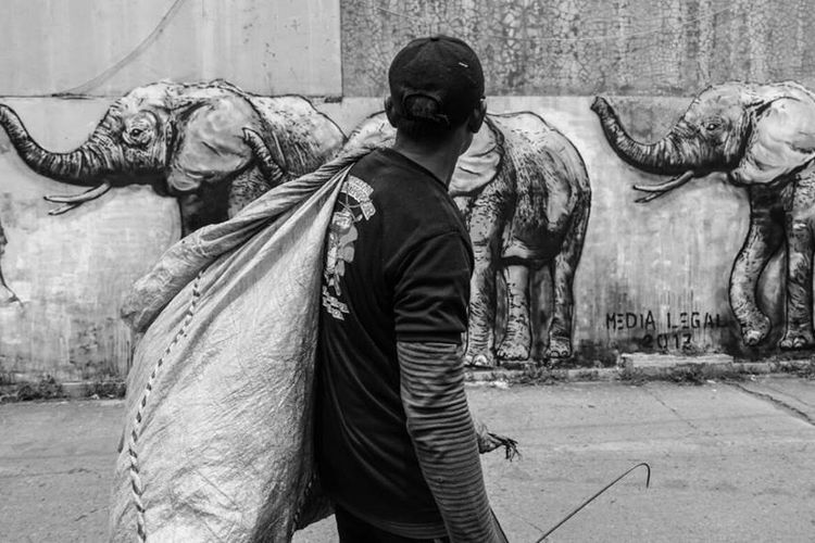 Seorang pemulung melintas di depan mural bergambar Gajah-Gajah di Festival Gang Abdul Jabar ke-2, 2017.