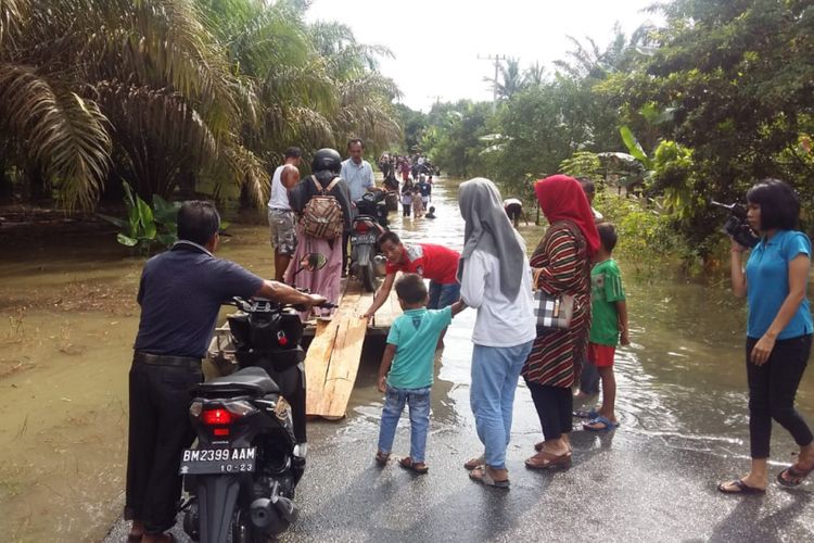 Sejumlah warga melintasi jalan yang terendam banjir di Kabupaten Kampar, Riau