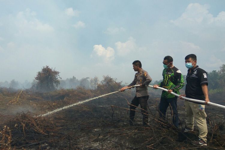 Petugas kepolisian dari Polresta Pontianak saat memadamkan kebakaran lahan yang terjadi di Sekunder C, Kecamatan Rasau Jaya, Kabupaten Kubu Raya  (24/7/2018).