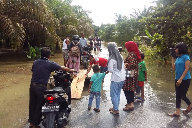 Sejumlah warga melindasi jalan yang terendam banjir di Kabupaten Kampar, Riau