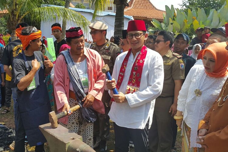 Wakil gubernur terpilih DKI Jakarta Sandiaga Uno menempa bilah tradisional saat datang ke acara Lebaran Betawi di PBB Setu Babakan, Jakarta Selatan, Minggu (30/7/2017).