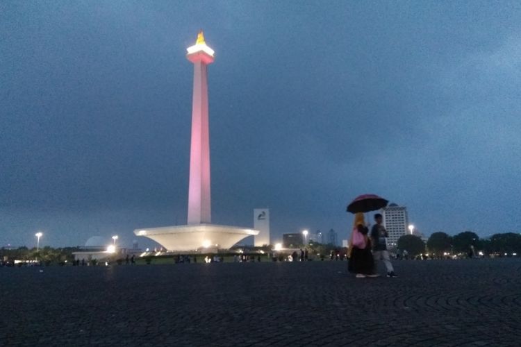 Pengunjung dengan latar belakang Tugu Monas di malam hari, Jumnat (15/6/2018).