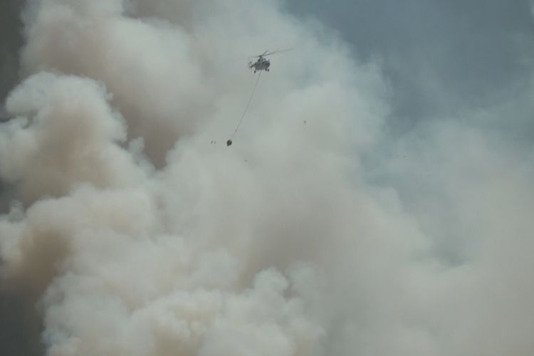 Sebuah helikopter terbang melintasi asap tebal untuk menyiramkan air ke lokasi kebakaran lahan  di Desa Sungai Rambutan, Ogan Ilir, Sumatra Selatan, Minggu (6/8/2017).