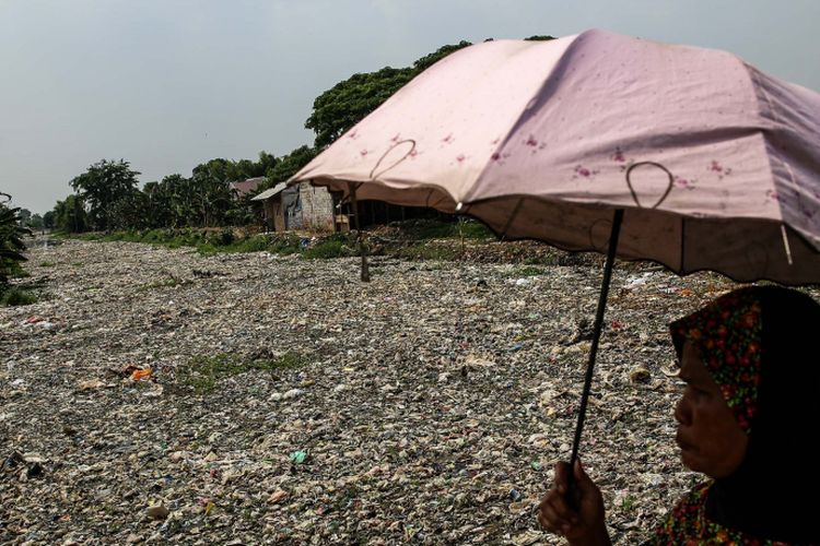 Warga melintas disamping sampah yang didominasi plastik di sepanjang Kali Pisang Batu, Desa Pahlawan Setia, Kecamatan Tarumajaya, Kabupaten Bekasi, Jawa Barat, Selasa (8/1/2019). Sampah yang memenuhi Kali Pisang Batu hingga sepanjang 1,5 kilometer berasal dari Kali Bekasi yang melewati Kota Bekasi. Sampah muncul pasca normalisasi dilakukan pada Desember 2018. Sebelumnya, kali hanya dipenuhi lumpur dan eceng gondok.