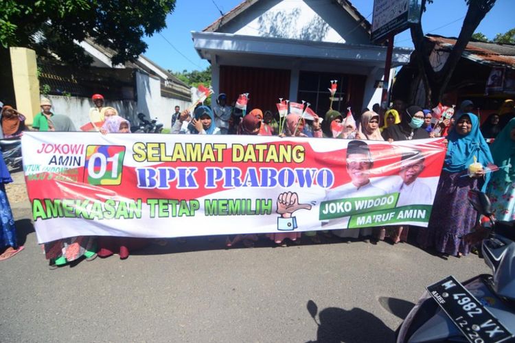 Aksi ibu-ibu di Pamekasan membentangkan spanduk dukungan kepada Jokowi-Maruf saat menyambut kedatangan Prabowo.