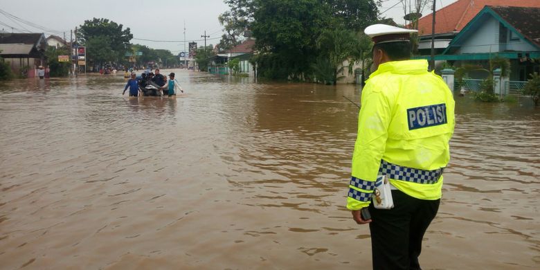 Seorang polisi sedang memantau kondisi jalur pantura di wilayah Kraton Pasuruan yang lumpuh total akibat genangan air setinggi satu meter.