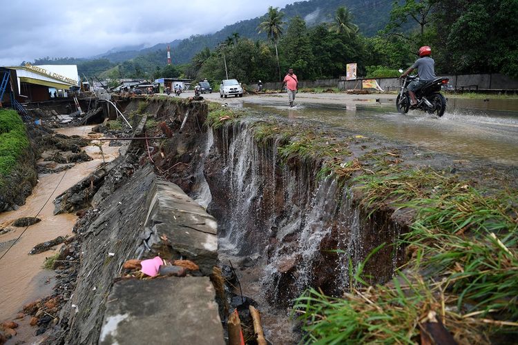 Warga melintasi di samping jalan yang rusak akibat banjir bandang di Sentani, Jaya Pura, Papua, Senin (18/3/2019). Akibat banjir bandang yang melanda Sentani sejak Sabtu (16/3) lalu, sedikitnya empat ribu warga mengungsi di sejumlah posko pengungsian. 