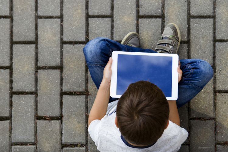 Boy with tablet outdoors. Child with pc computer sitting on the pavement. Top view. Technology, computer addiction, education concept