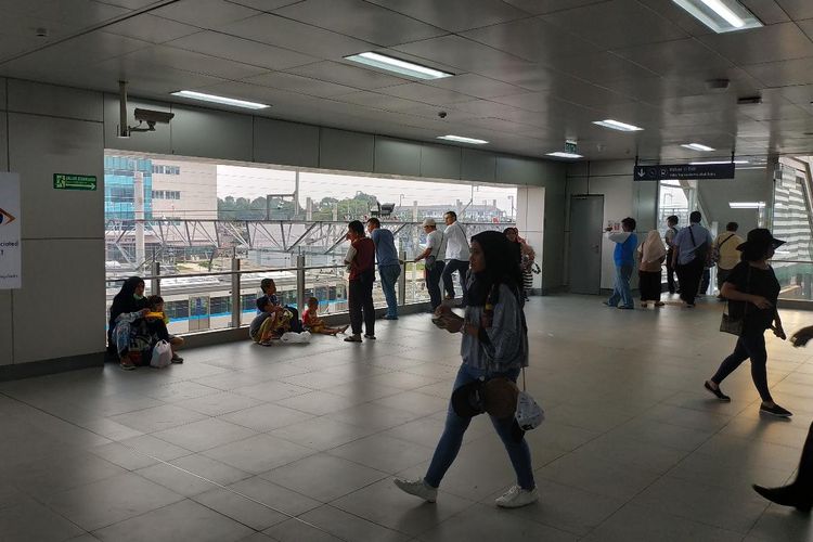 Beberapa penumpang di Stasiun MRT Lebak Bulus duduk di lantai area luar gerbang pembayaran pada Selasa (9/4/2019). Sebagian besar menyebut, tindakan mereka didasari oleh ketiadaan kursi di area tersebut, padahal antrean loket mengular panjang.