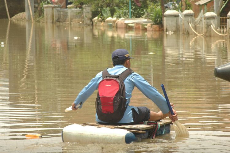 Seorang pelajar di Kabupaten Bandung tengah menyebrangi banjir yang merendam wilayahnya dengan menggunakan perahu rakitan dari jerigen dan kayu.