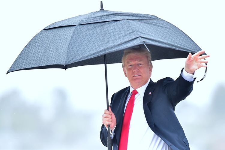 Presiden AS Donald Trump melambai sambil memegang payungnya saat tiba di Los Angeles, California, Selasa (13/3/2018). (AFP/Frederic J Brown)