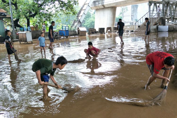 Anak-anak membersihkan lumpur menggunakan sapu lidi pasca-banjir di kolong Flyover Rawajati, Jakarta Selatan, Selasa (6/2/2018).