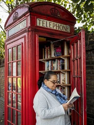 Penduduk setempat, Patsy Ari melihat-lihat buku di sebuah boks telepon merah yang berubah menjadi perpustakaan di Lewisham Way, di London selatan. Foto ini diambil pada 21 Oktober 2017. (AFP/Tolga Akmen)