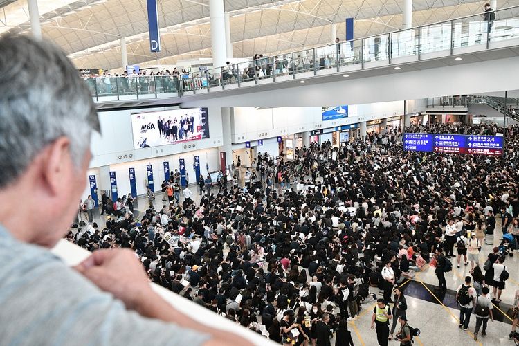 Seorang pengunjung melihat massa pengunjuk rasa yang melakukan aksi duduk di aula kedatangan Bandara Internasional Hong Kong, Jumat (9/8/2019).
