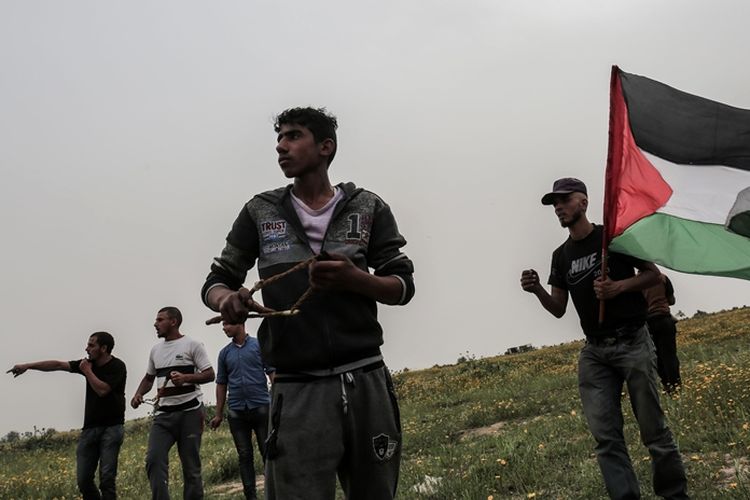 Warga Palestina melempar batu menggunakan ketapel ke arah pasukan Israel saat terjadinya gesekan dalam aksi di perbatasan Israel di Khan Yunis, selatan Jalur Gaza, 23 Maret 2018.